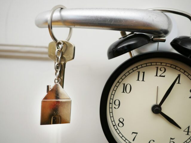 Key hanging on door with silver home key ring - vintage alarm clock in background.