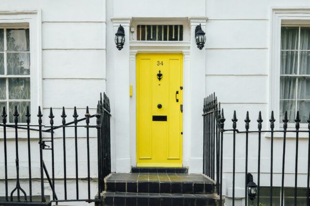 yellow front door with lock and white walls and iron fence